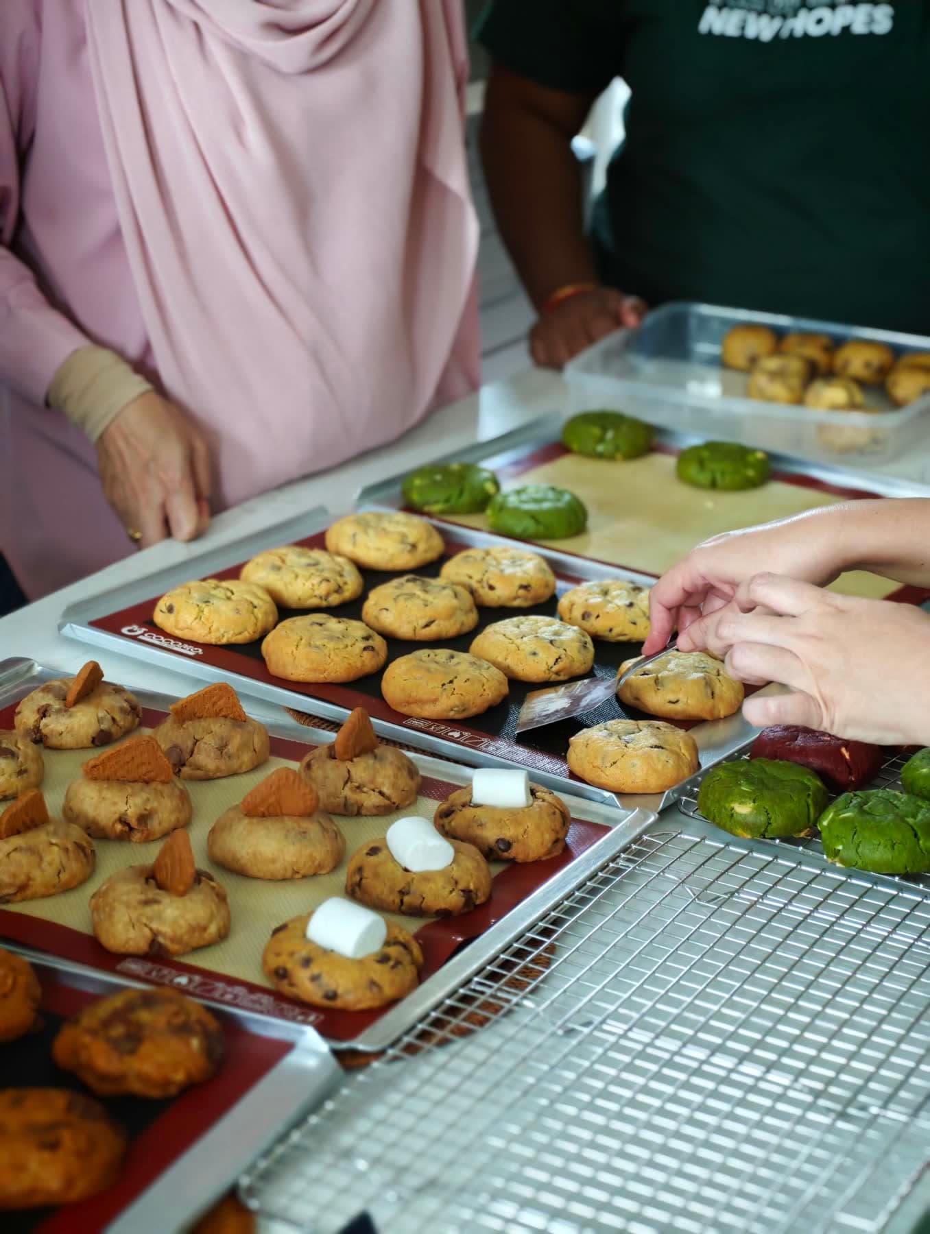 Hands finishing trays of thick chocolate chip, Biscoff, s'mores, and matcha cookies at the NYC Cookies class