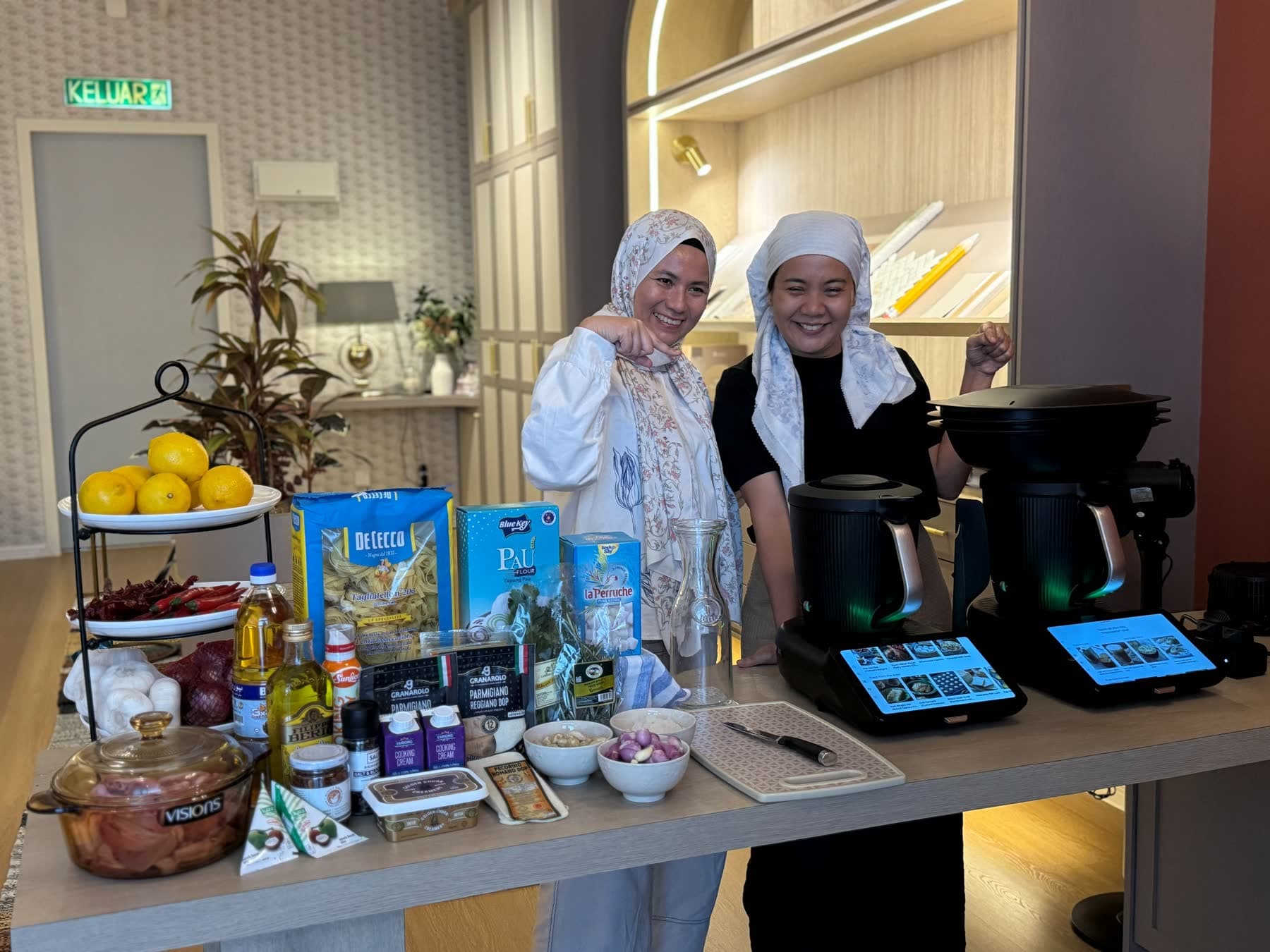 Two CooknShare instructors behind the Western Cooking mise en place — pasta, Parmigiano, lemons, and two Thermomix® machines